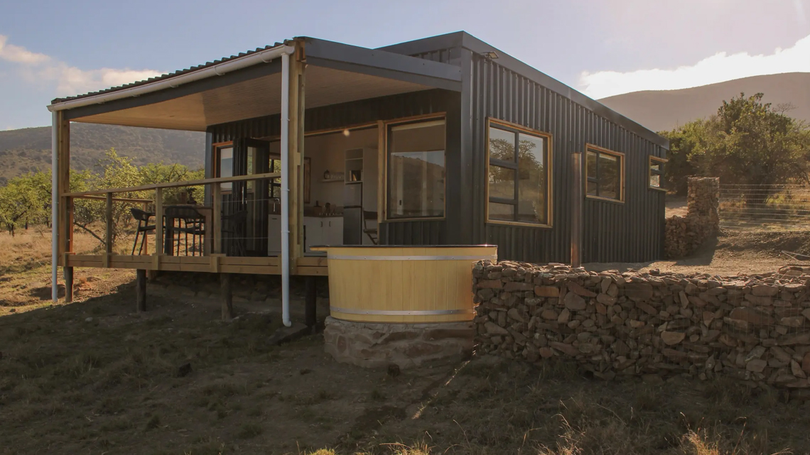 Luxury modern farm cabin built by Prism Construction in Somerset East, featuring a private wooden deck and a smoking wood-fired hot tub overlooking the landscape.